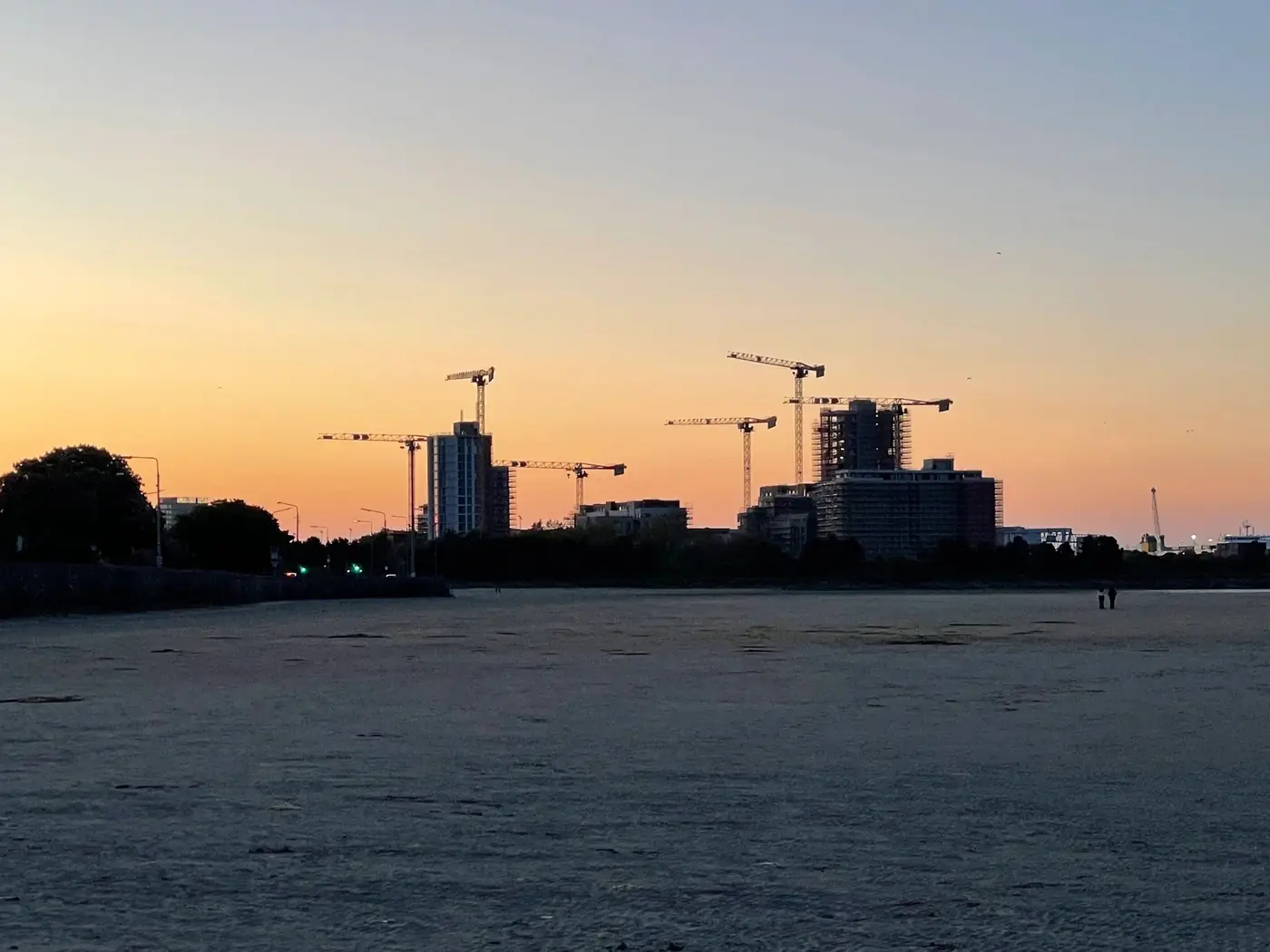 Tower cranes on the skyline at sunset, seen across an open field