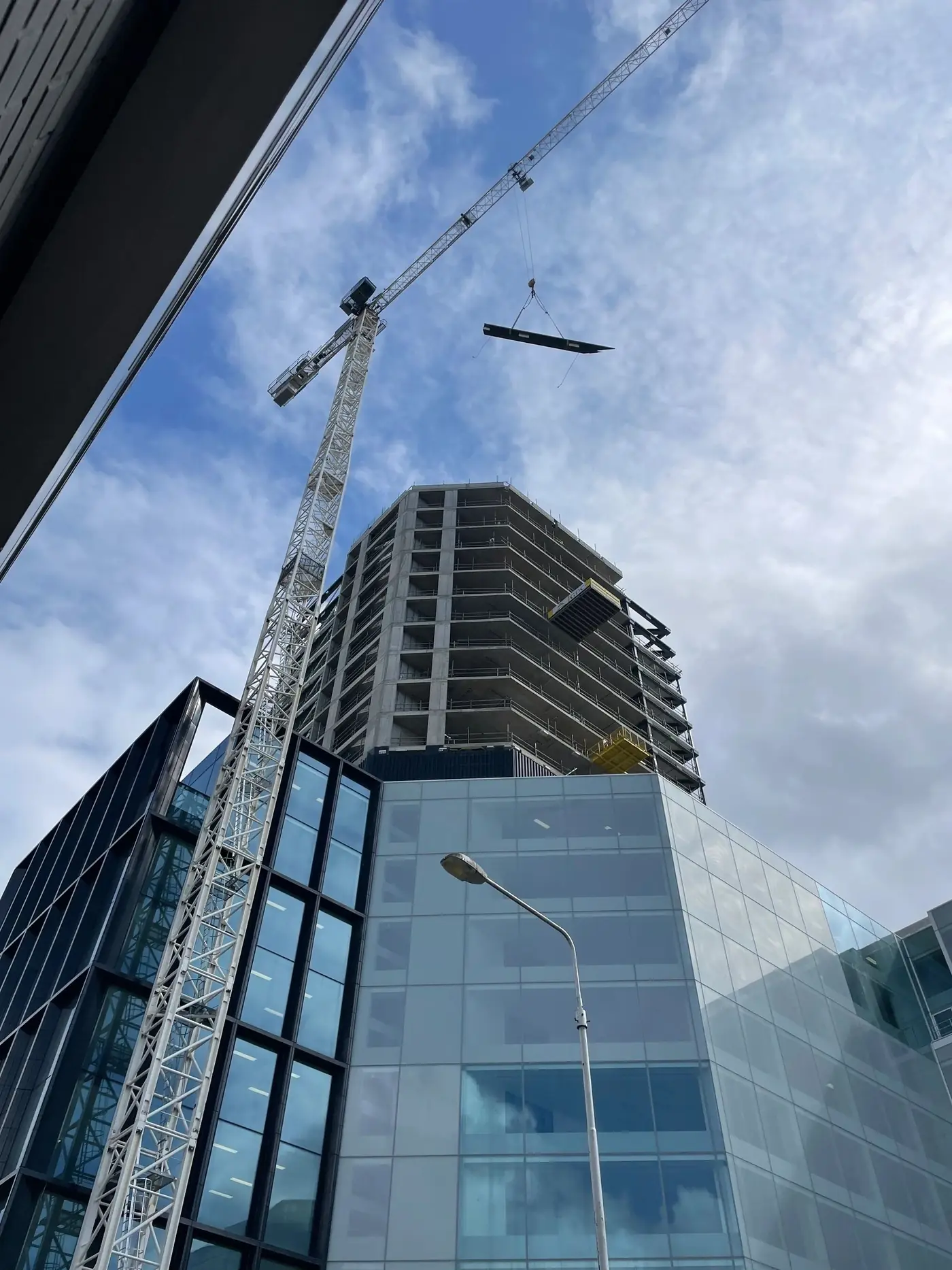 A tower crane lifting steel over a glass office building